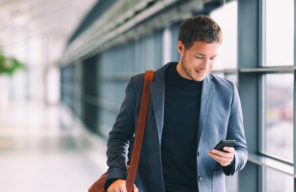 Man holding phone - young businessman using smartphone in airport. Casual urban professional business man texting cellphone happy inside office banner panorama with copy space on background.